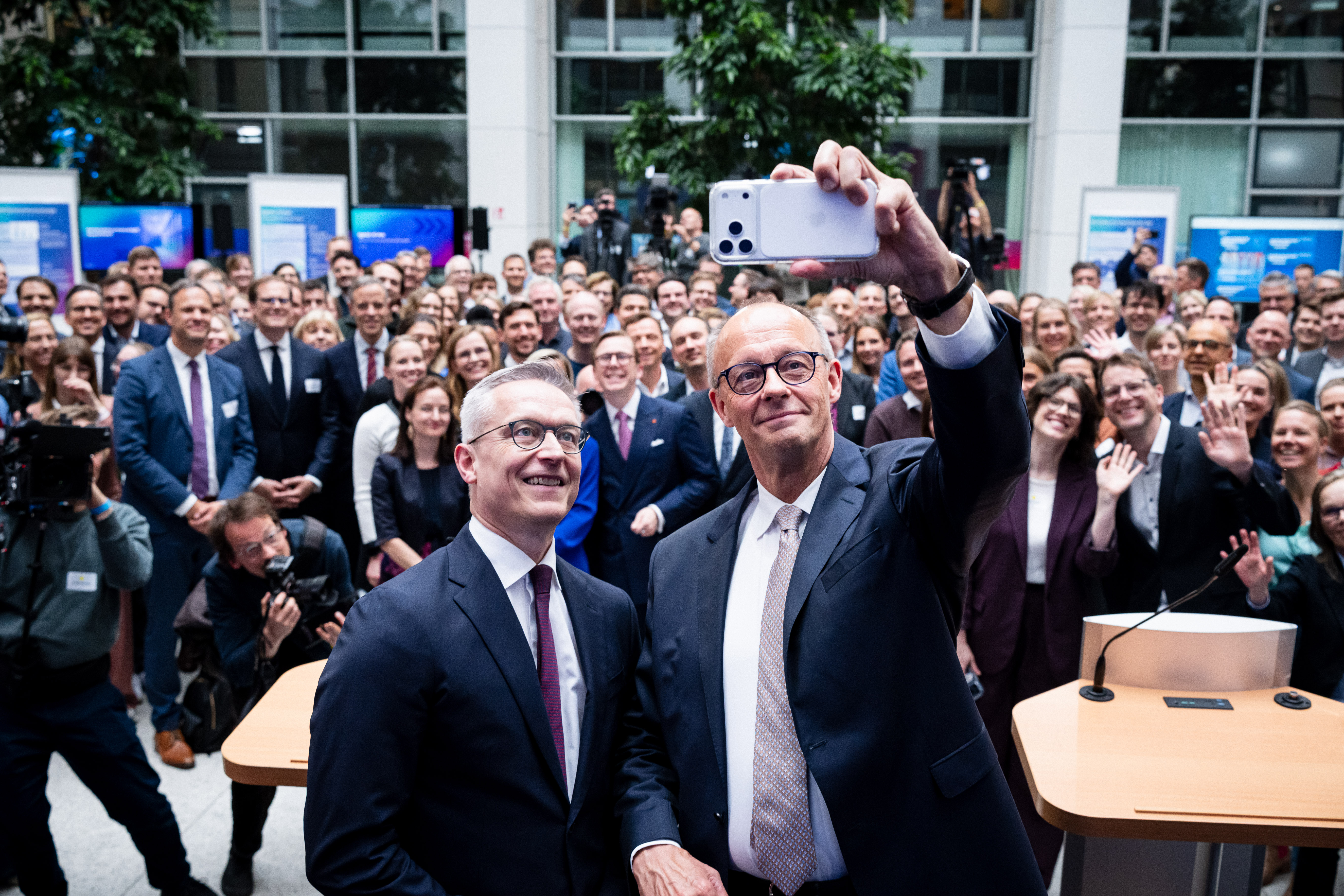 Karsten Wildberger und Friedrich Merz machen ein Selfie. Hinter ihnen steht eine große Menschenmenge, einige Personen winken.