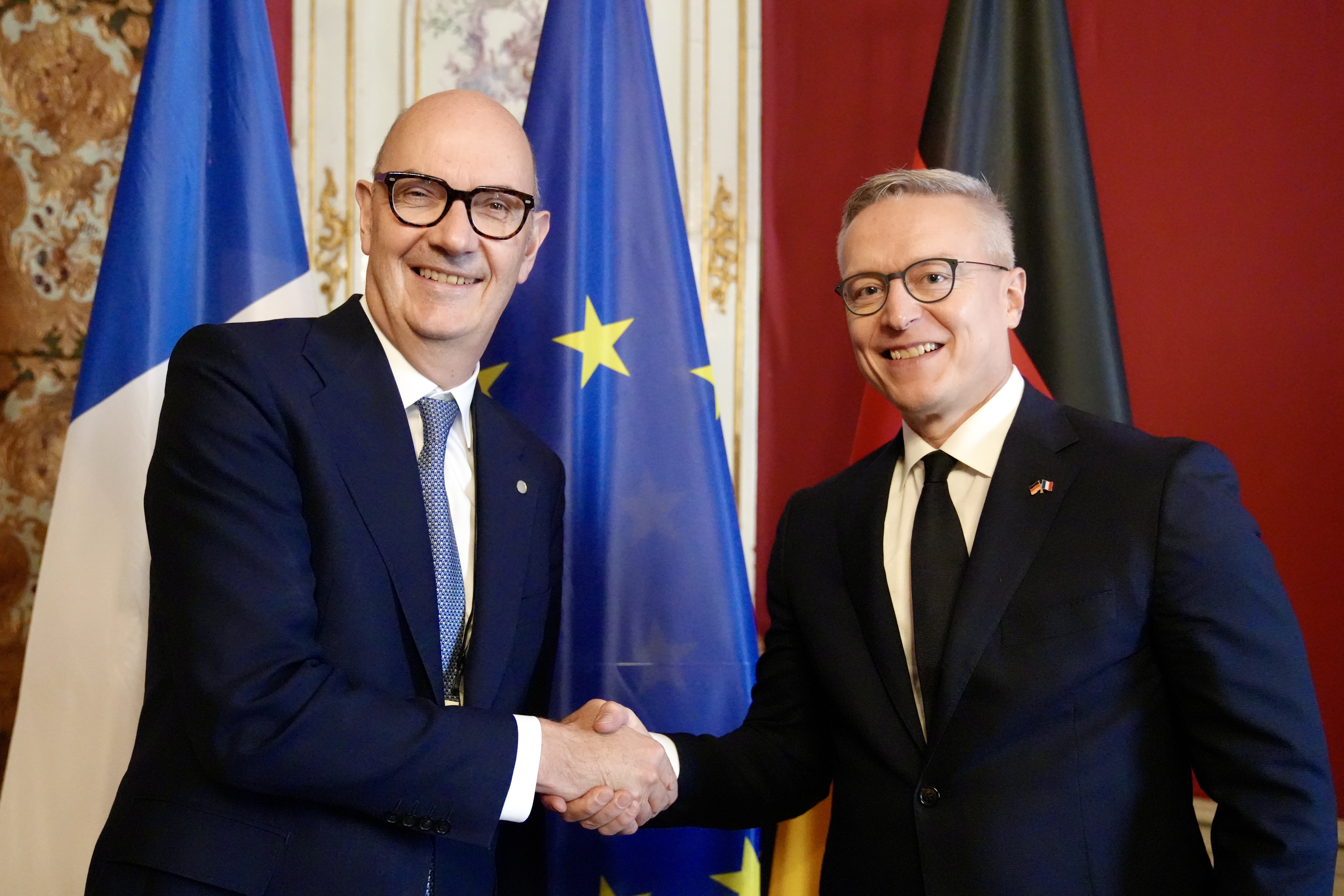Der französische Finanzminister Roland Lescure und Karsten Wildberger geben sich die Hand. Im Hintergrund sind die Flaggen Frankreichs, Deutschlands und der Europäischen Union zu sehen.