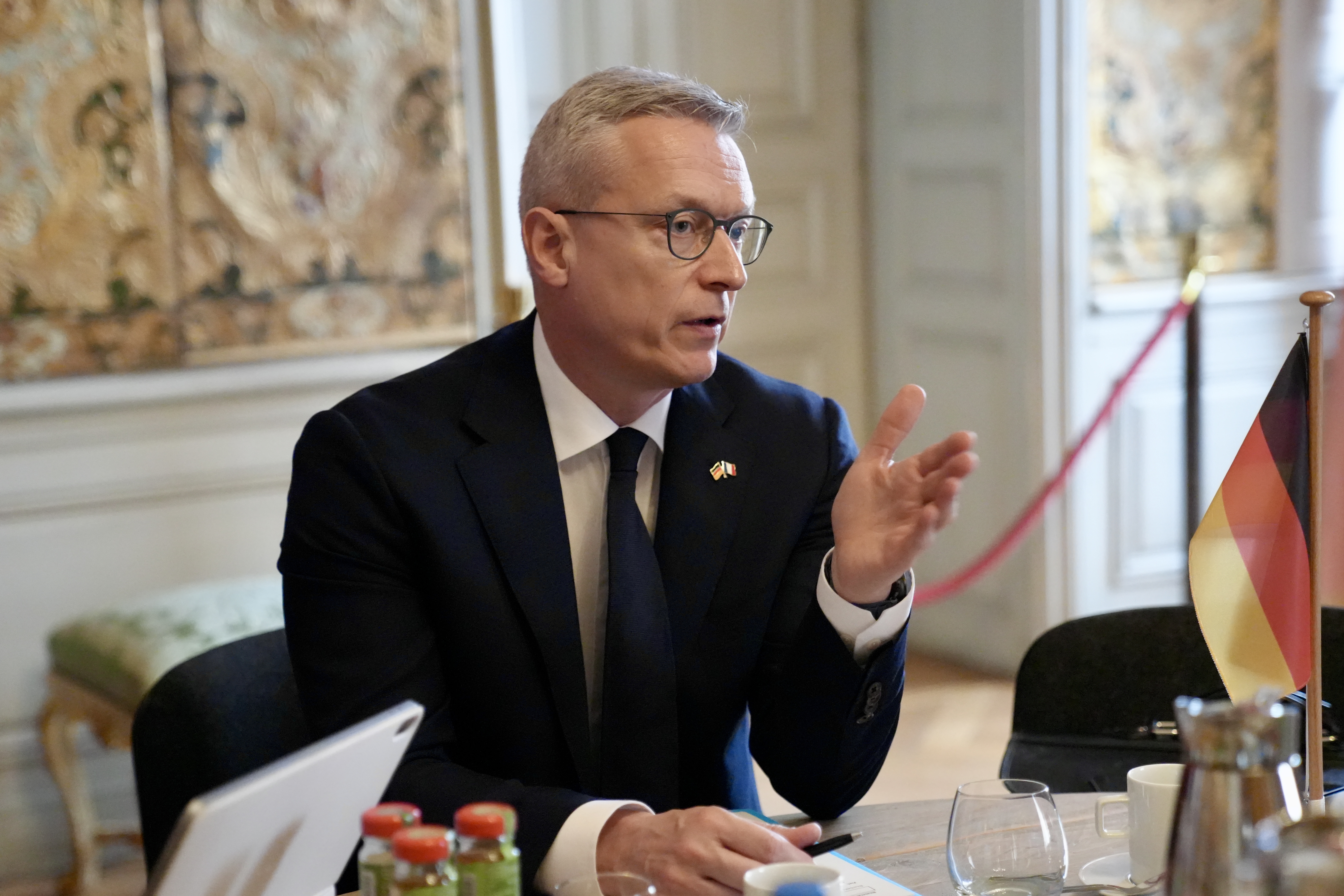 Karsten Widlberger sitzt an einem Besprechungstisch und spricht mit ausgestreckter Hand.