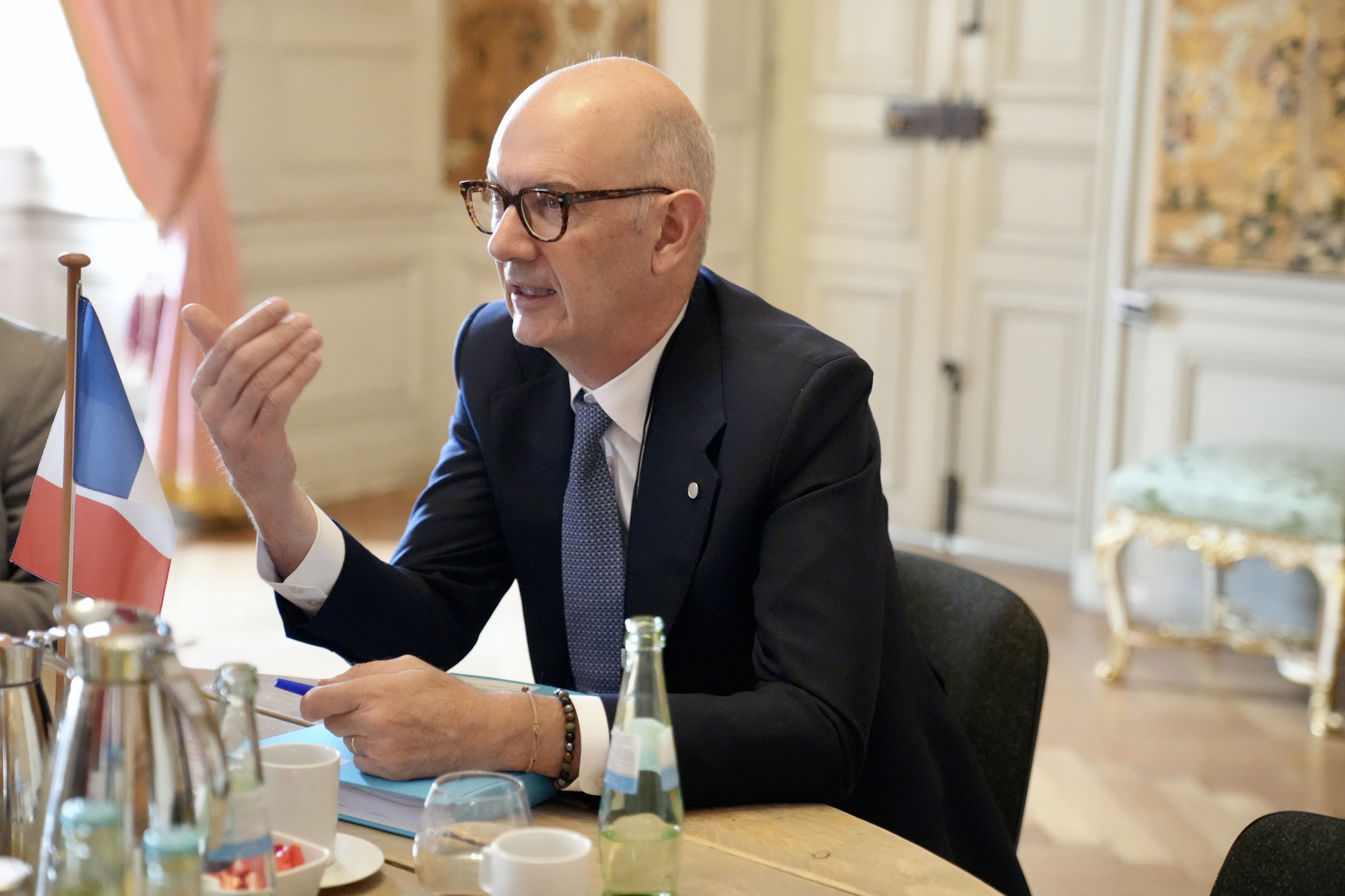 Der französische Finanzminister Roland Lescure sitzt an einem Besprechungstisch und spricht mit ausgestreckter Hand.