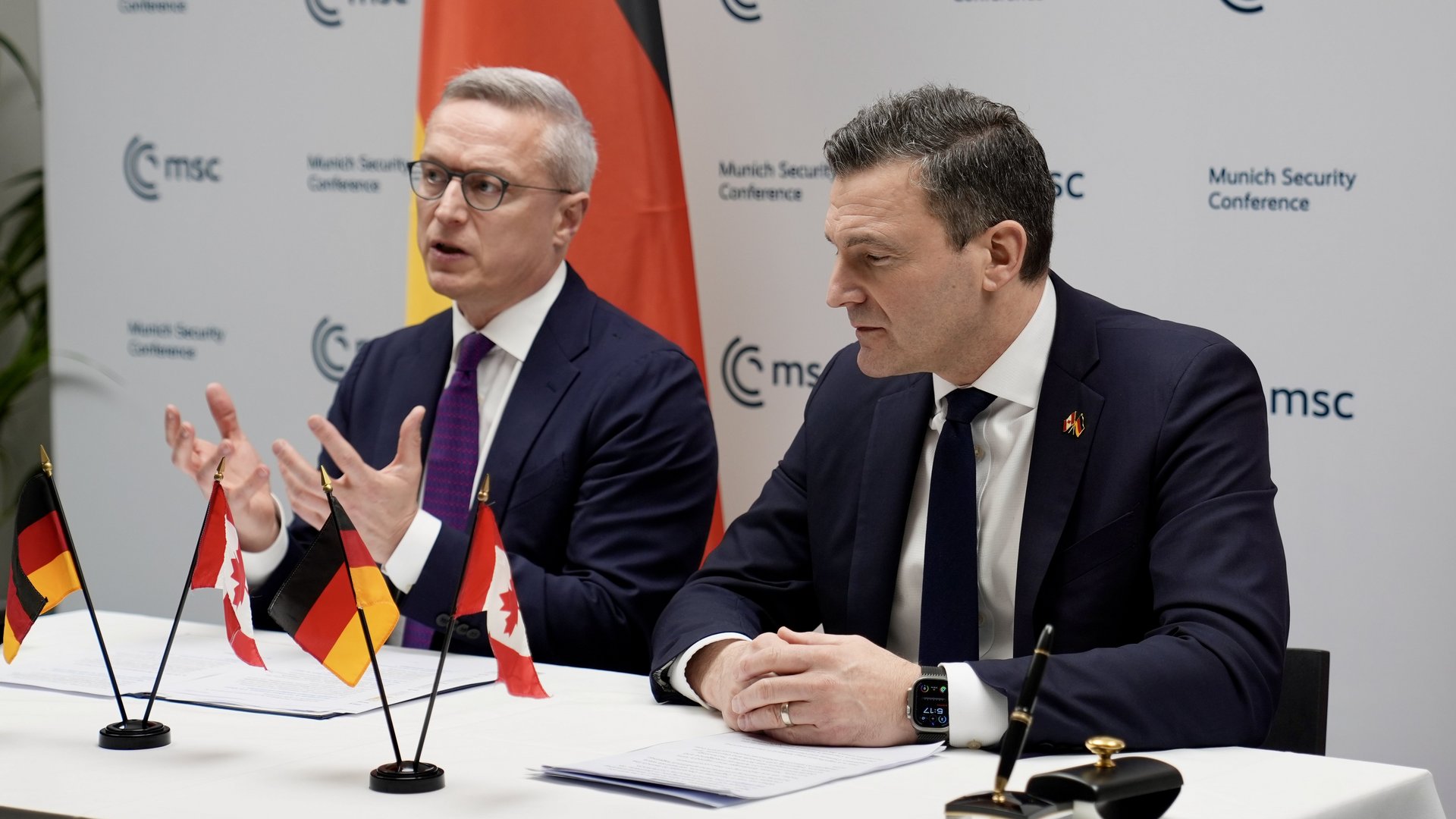Der deutsche und der Kanadische Minister sitzen an einem Tisch. Auf dem Tisch stehen die deutsche und die kanadische Flagge.