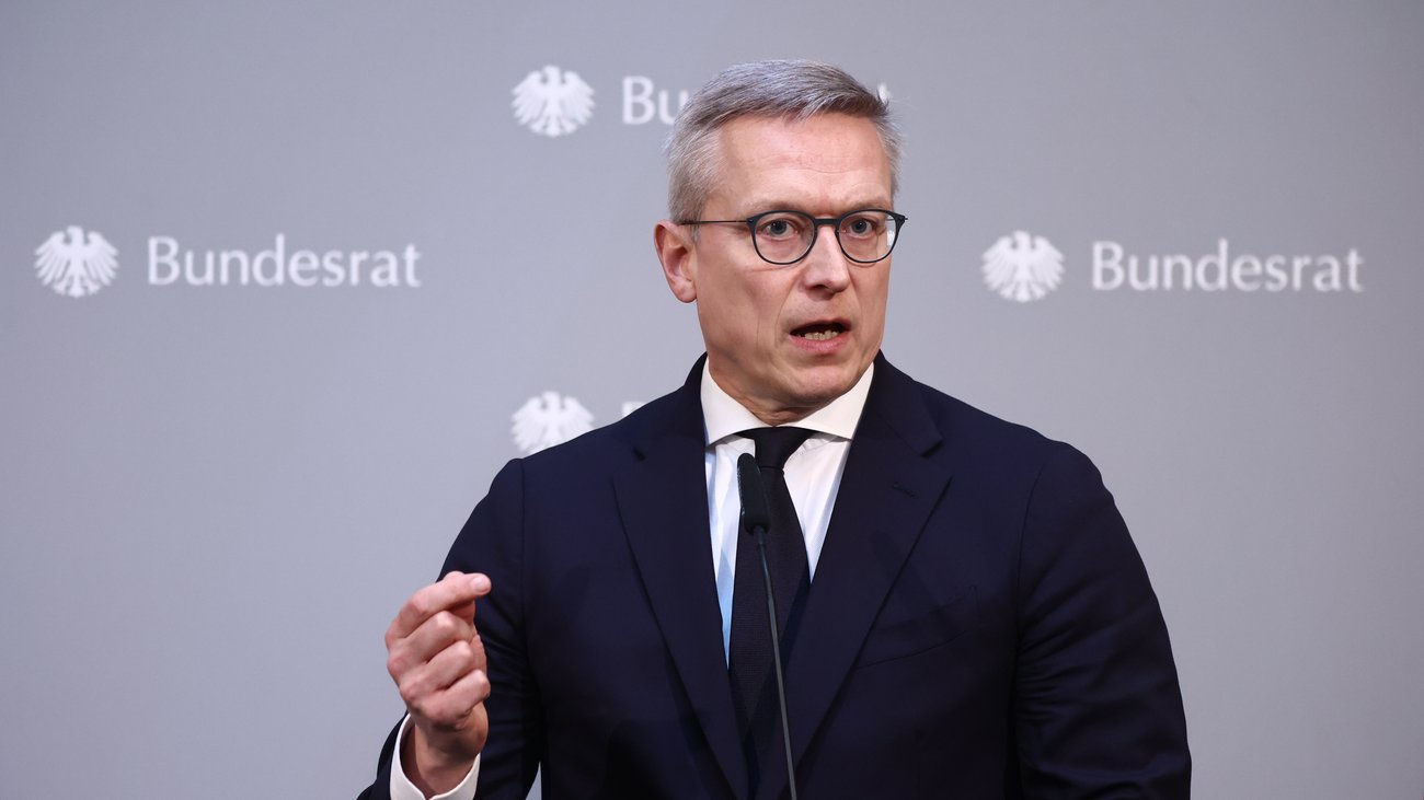 Nahmaufnahme eines Mannes in einem schwarzen Anzug, der vor einer Pressewand mit der Aufschrift Bundesrat redet. 