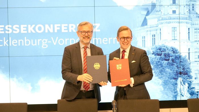 Amthor und Geue halten vor einer Pressewand die unterzeichneten Dokumente in die Kamera. 