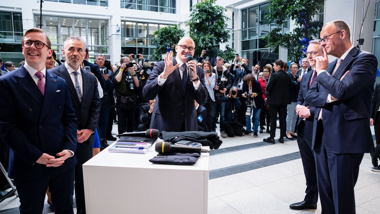 Hagen Saxowski spricht in ein Mikrofon und gestikuliert. Links von ihm stehen Philipp Amthor und Thomas Jarzombek, rechts von ihm stehen Karsten Wildberger und Friedrich Merz. Im Hintergrund sind Fotografen zu sehen.