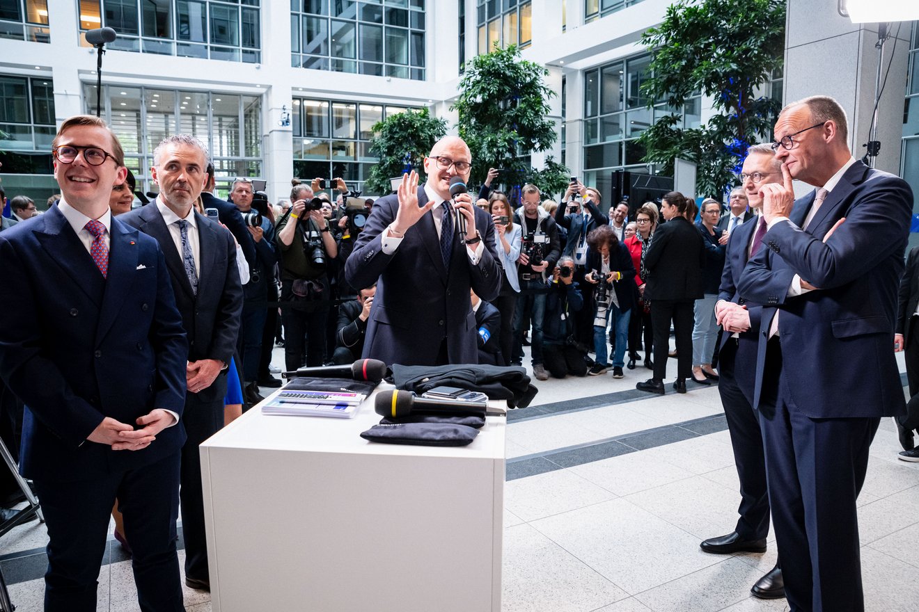 Hagen Saxowski spricht in ein Mikrofon und gestikuliert. Links von ihm stehen Philipp Amthor und Thomas Jarzombek, rechts von ihm stehen Karsten Wildberger und Friedrich Merz. Im Hintergrund sind Fotografen zu sehen.