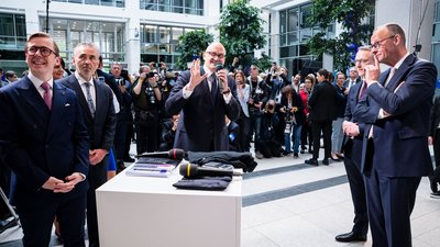Hagen Saxowski spricht in ein Mikrofon und gestikuliert. Links von ihm stehen Philipp Amthor und Thomas Jarzombek, rechts von ihm stehen Karsten Wildberger und Friedrich Merz. Im Hintergrund sind Fotografen zu sehen.
