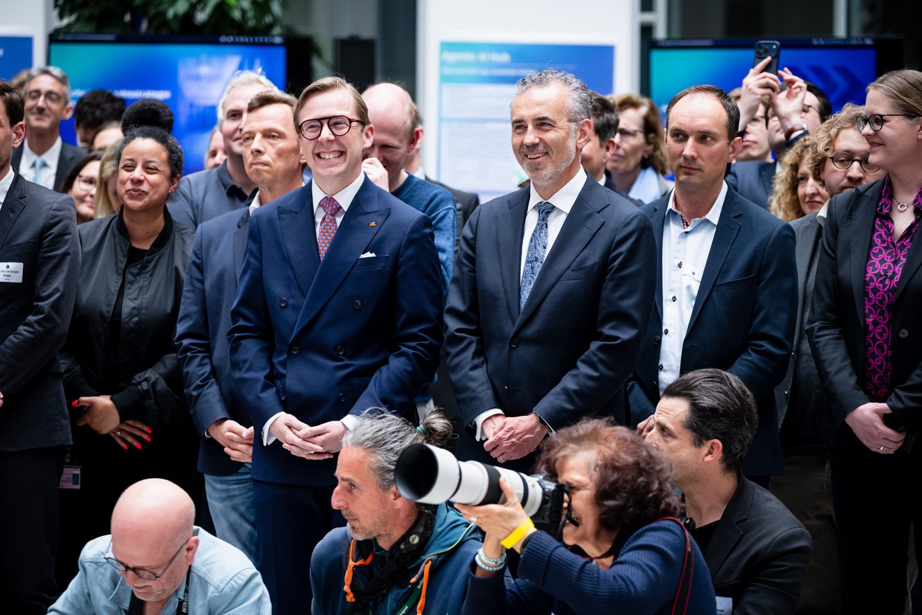 Philipp Amthor und Thomas Jarzombek stehen lächelnd in einer Gruppe von Menschen bei einer Veranstaltung. Im Vordergrund sind Fotografen mit professionellem Kamera-Equipment zu sehen, die die Szene dokumentieren.