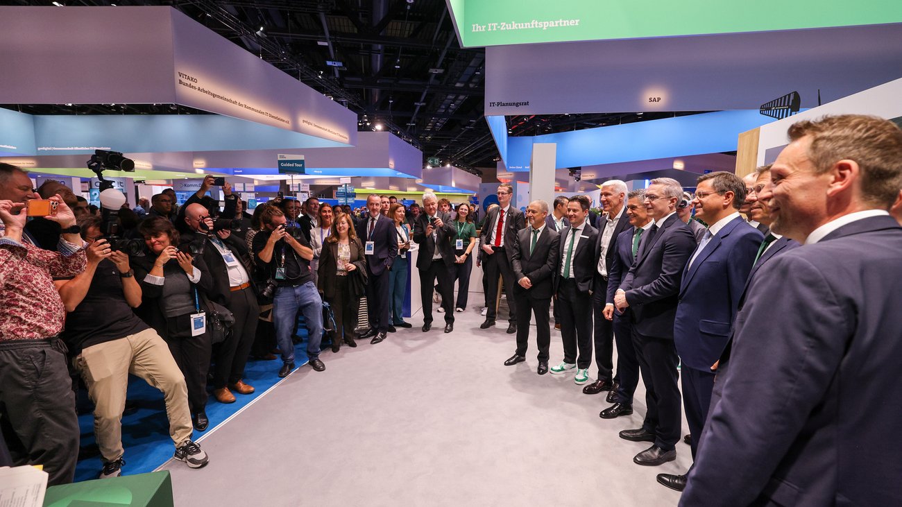 Auf einer Messe nehmen mehrere Fotografinnen und Fotografen ein Gruppenbild von Männern in Anzügen auf