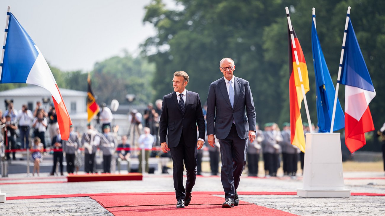 Frankreichs Präsident Emmanuel Macron und Bundeskanzler Friedrich Merz gehen über einen roten Teppich.