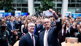 Karsten Wildberger und Friedrich Merz machen ein Selfie. Hinter ihnen steht eine große Menschenmenge, einige Personen winken.