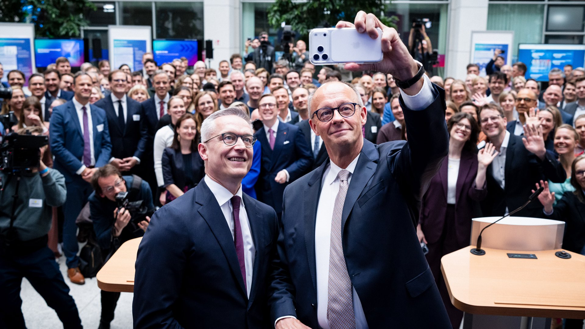 Karsten Wildberger und Friedrich Merz machen ein Selfie. Hinter ihnen steht eine große Menschenmenge, einige Personen winken.