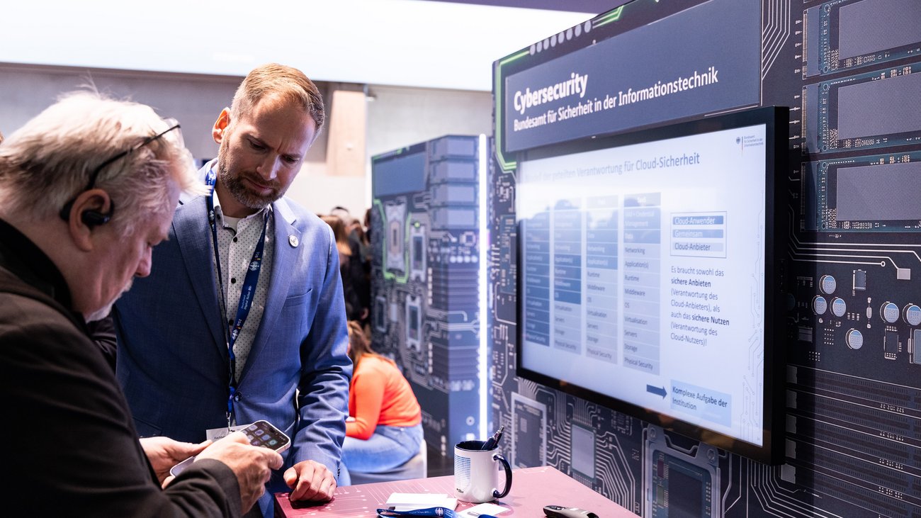 2 Personen an einem Messestand zu Cybersecurity. 
