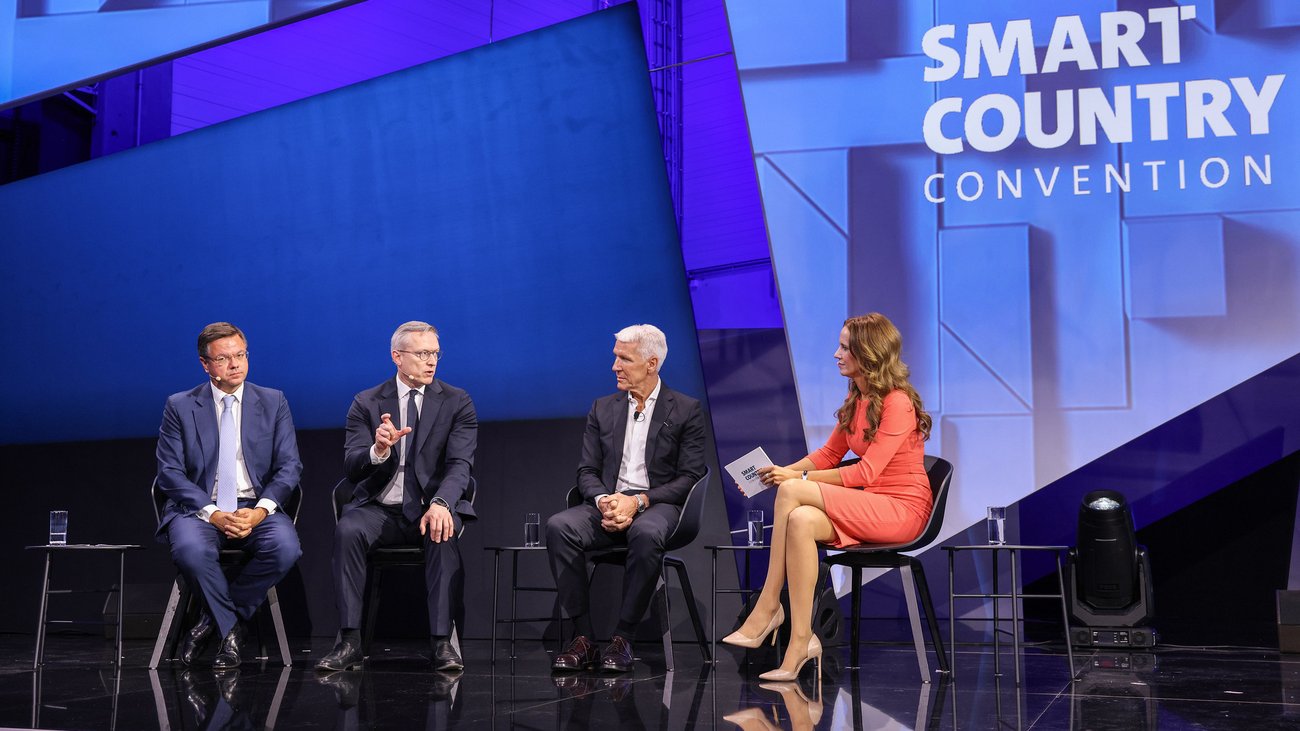 Drei Männer und eine Frau sitzen auf einer Bühne der Smart Country Convention und diskutieren. 