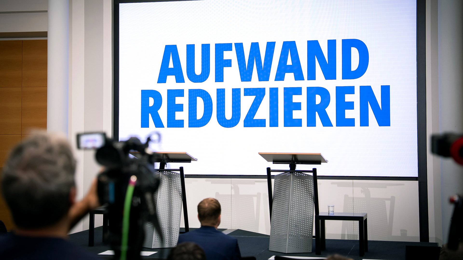 Leinwand vor Podium mit Schriftzug "Aufwand reduzieren"