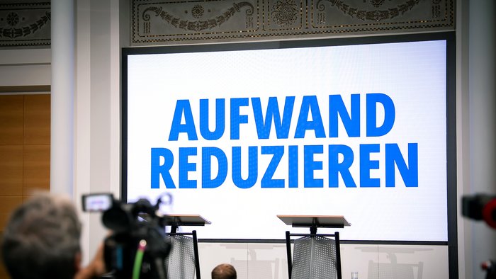 Leinwand vor Podium mit Schriftzug "Aufwand reduzieren"