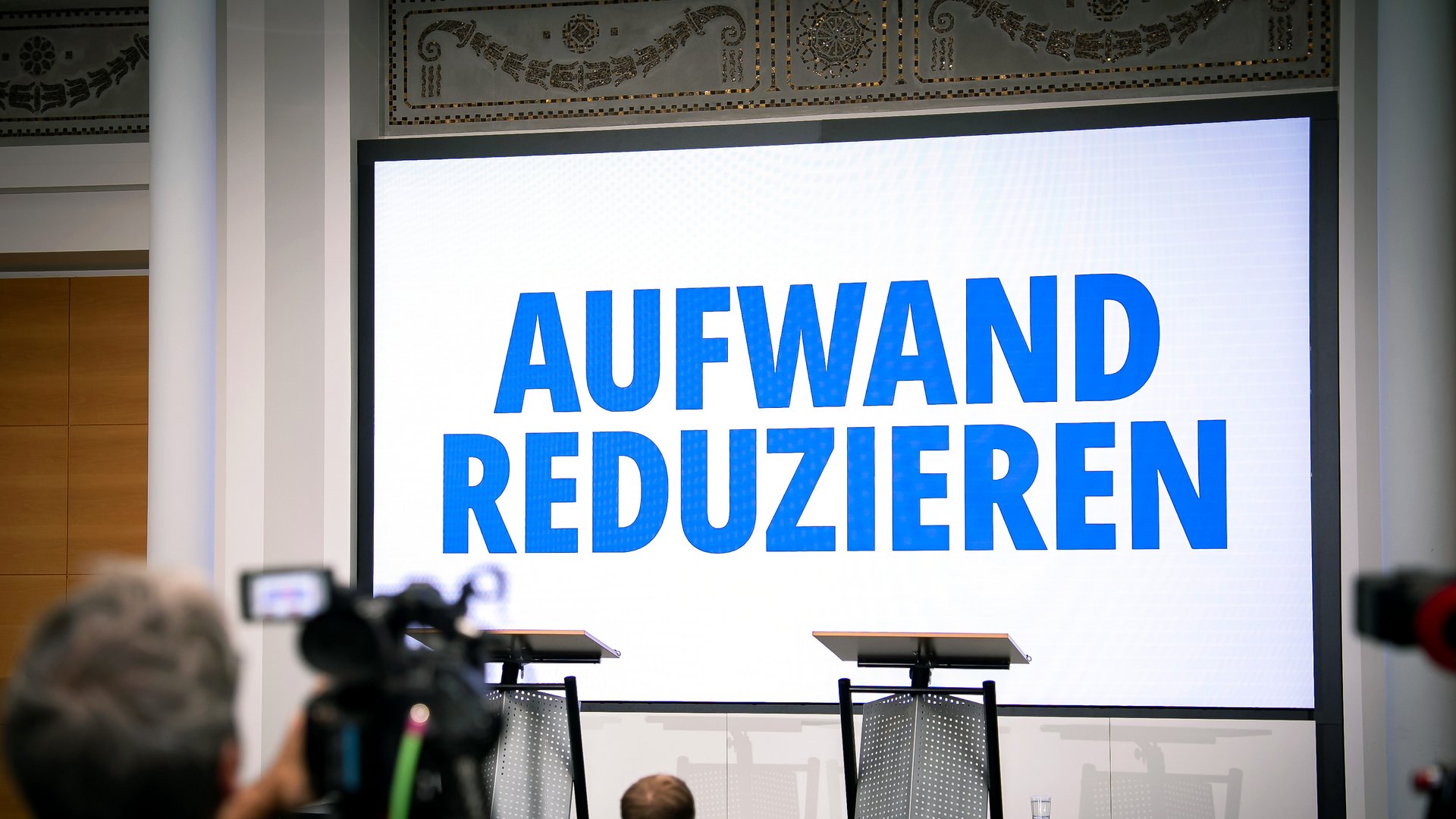 Leinwand vor Podium mit Schriftzug "Aufwand reduzieren"