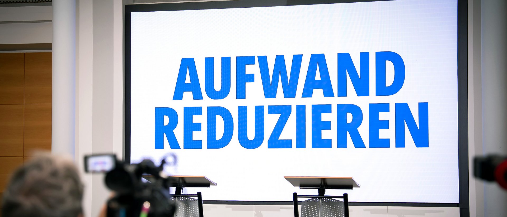 Leinwand vor Podium mit Schriftzug "Aufwand reduzieren"