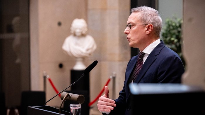 Seitliche Aufnahme von Bundesminister Wildberger an einem Rednerpult. Im Hintergrund eine Statue.
