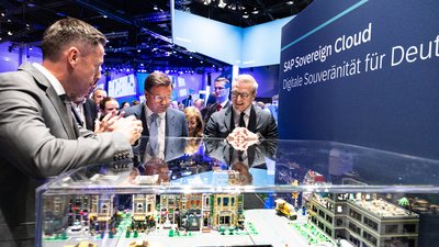 Mehrere Personen schauen an einem Messestand eine mit Bausteinen nachgebildete Stadt in einer Vitrine an