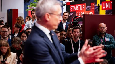 Verschwommener Blick auf Digitalminister Wildberger vor einem Messepublikum und dem Schriftzug „Startup Germany.“