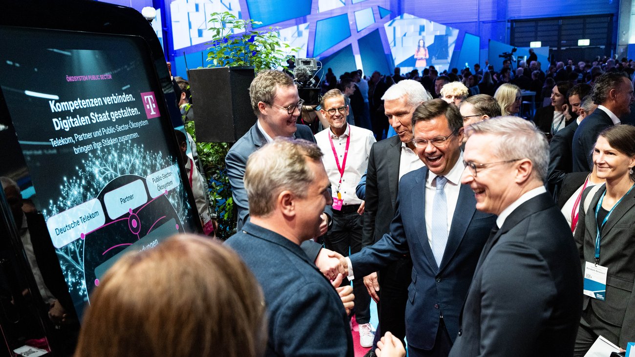 Mehrere männliche Messebesucher begrüßen sich mit Händeschütteln am Stand der Deutschen Telekom