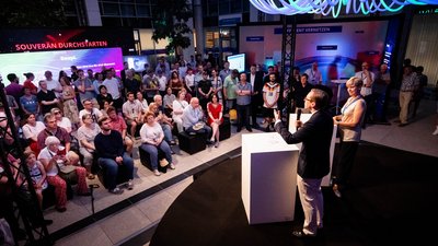 Blick ins Atrium, auf der Bühne ein Speaker. Der Raum ist gut gefüllt. 