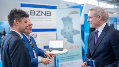 Bundesdigitalminister Dr. Karsten Wildberger und weitere Personen an einem Messestand der ANGA COM