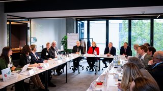 Foto eines Sitzungsraums des GovTech-Campus. Ca. 30 Mitglieder der Sozialstaatskommission sitzen U-förmig und diskutieren. 