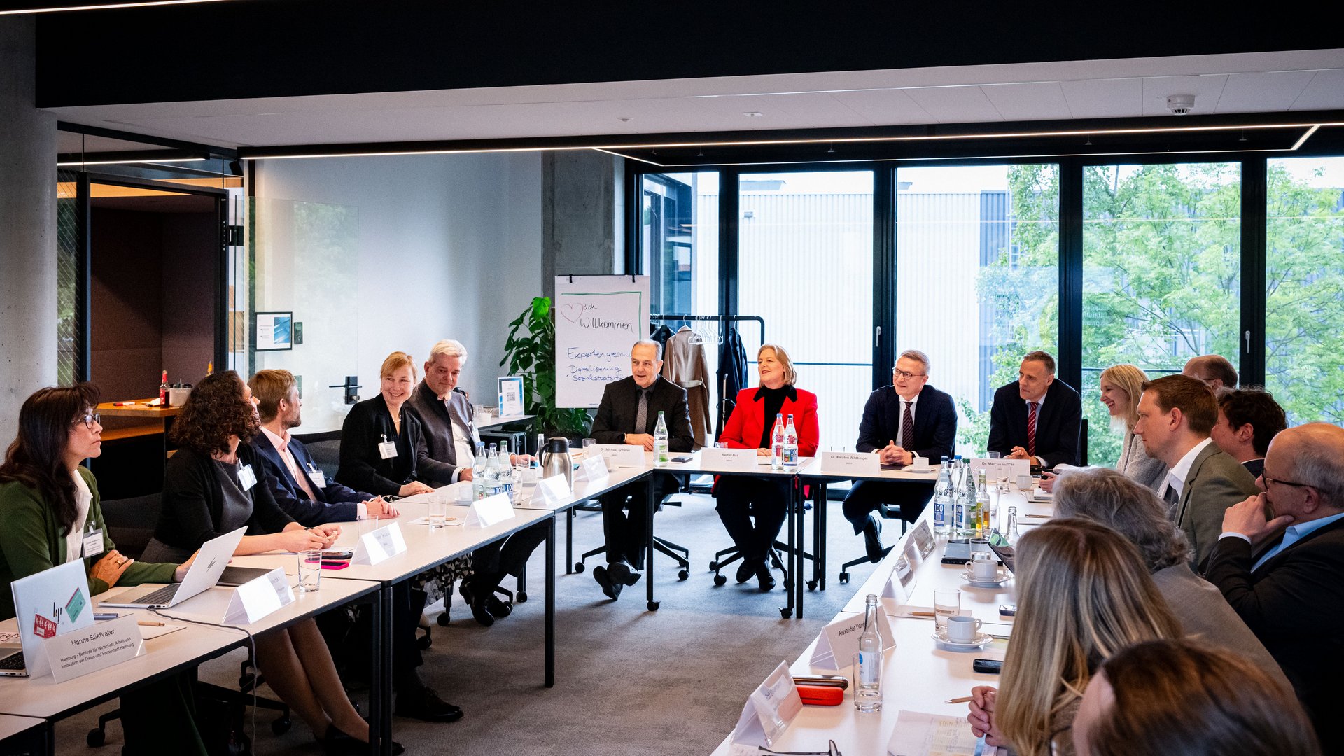 Foto eines Sitzungsraums des GovTech-Campus. Ca. 30 Mitglieder der Sozialstaatskommission sitzen U-förmig und diskutieren.