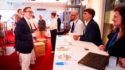 Standbesuch: Links Philipp Amthor im schwarzen Anzug, rechts hinter dem Tresen 3 Mitarbeitende der Start-ups vor Ort. 