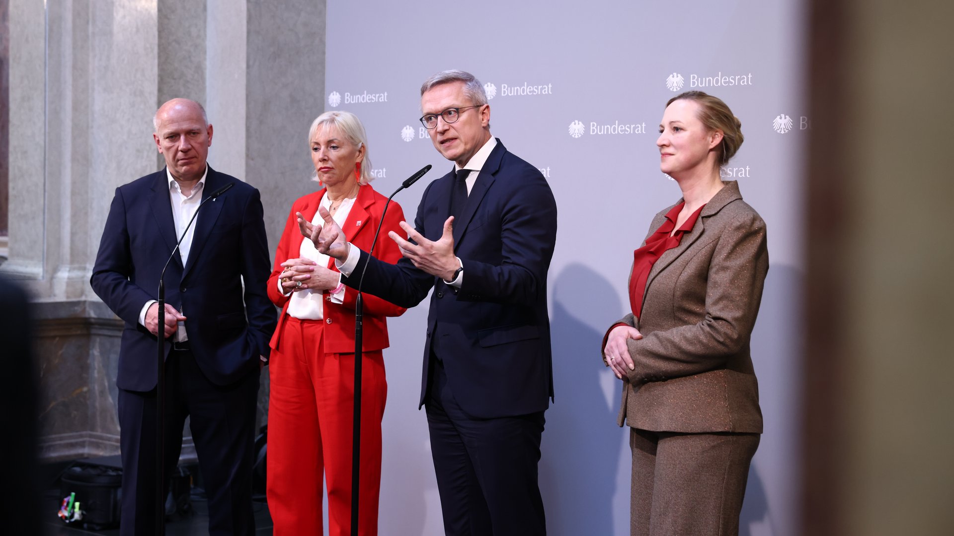 Zwei Männer und zwei Frauen in Business-Kleidung stehen vor einer Pressewand, die den Schriftzug Bundesrat trägt. Einer der Männer redet gerade und gestikuliert dabei mit den Händen.