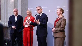 Zwei Männer und zwei Frauen in Business-Kleidung stehen vor einer Pressewand, die den Schriftzug Bundesrat trägt. Einer der Männer redet gerade und gestikuliert dabei mit den Händen. 