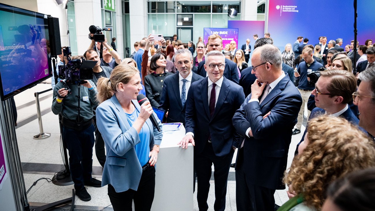 Claudia Straub spricht in ein Mikrofon, neben ihr stehen Friedrich Merz, Karsten Wildberger und Thomas Jarzombek. Im Hintergrund sind weitere Personen zu sehen.