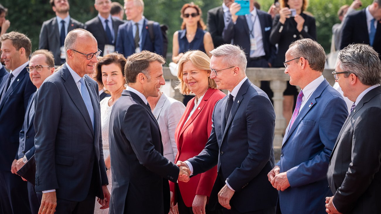 Bundesdigitalminister Karsten Wildberger begrüßt Frankreichs Präsidenten Emmanuel Macron geben sich die Hand. Um sie herum stehen weitere Mitglieder der Delegationen und Gäste.