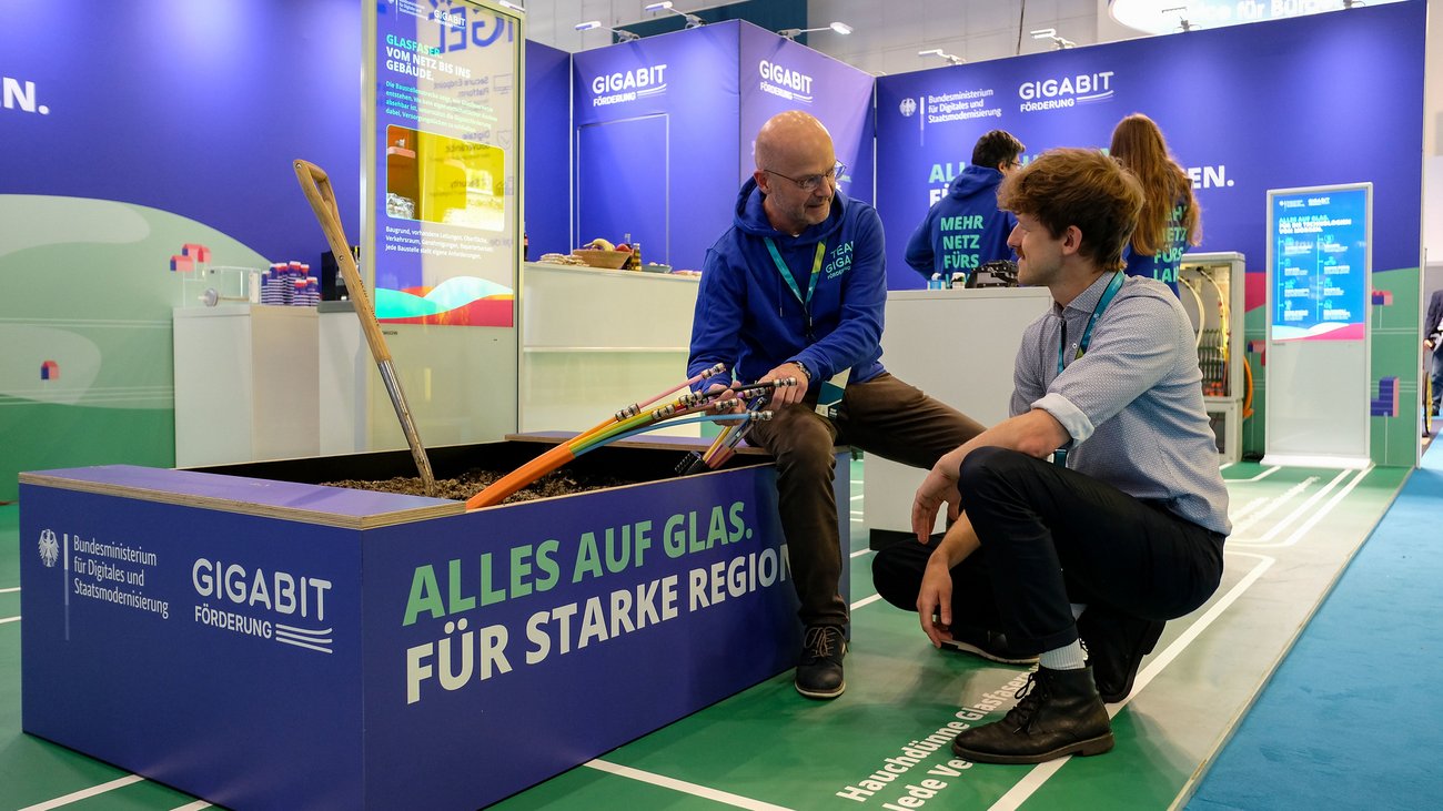Messestand mit zwei Männern im Gespräch neben Glasfaserkabeln