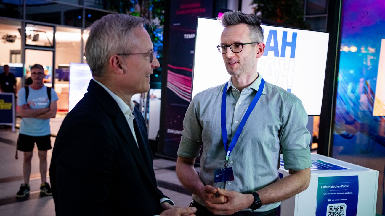 Minister Wildberger spricht mit einem Mann mit Messe-Badge an einem Stand