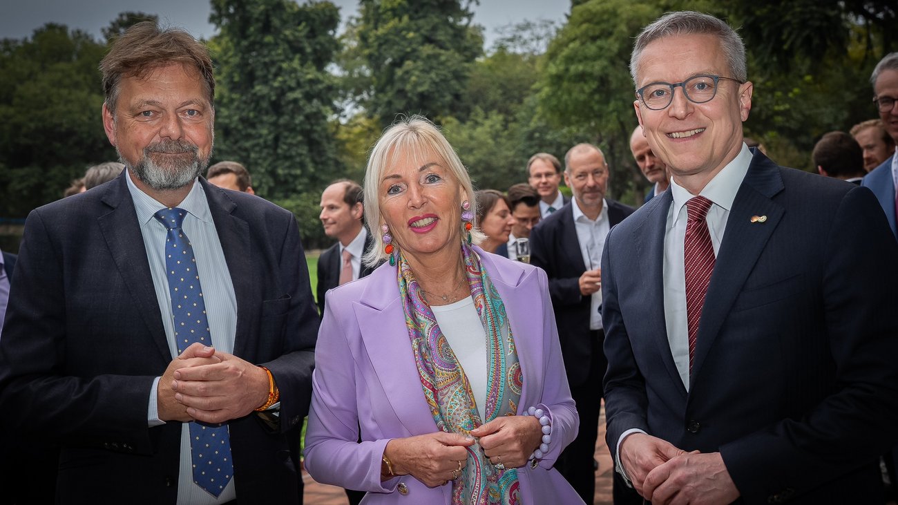 3 Menschen in Business-Kleidung – 2 Männer und eine Frau – stehen für ein Foto bereit. 