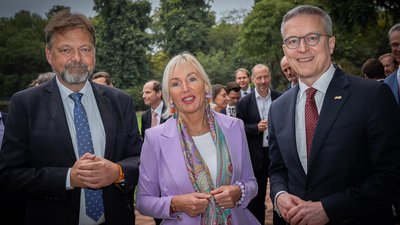 3 Menschen in Business-Kleidung – 2 Männer und eine Frau – stehen für ein Foto bereit. 