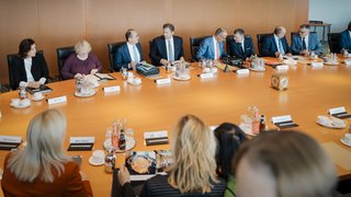 Blick in die Kabinettssitzung: Viele Männer und Frauen in Business-Kleidung sitzen am runden Kabinettstisch. 