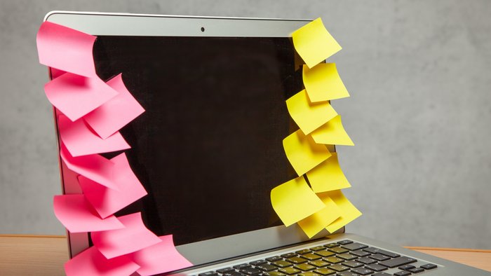 Ausgeschaltetes Notebook vollgeklebt mit unbeschrifteten gelben und rosa Klebezetteln