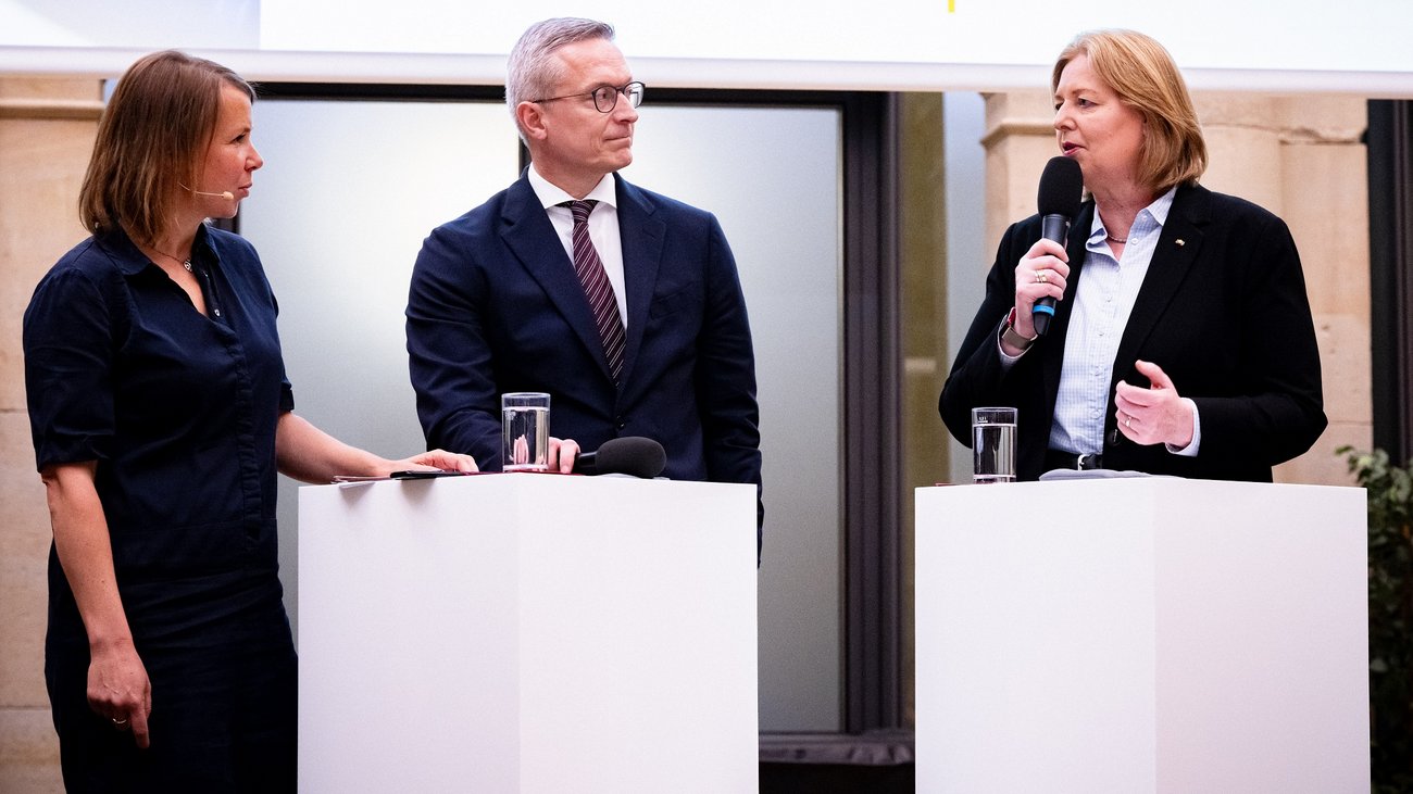 Eine Moderatorin im Gespräch mit Dr. Karsten Wildberger und Bärbel Bas.