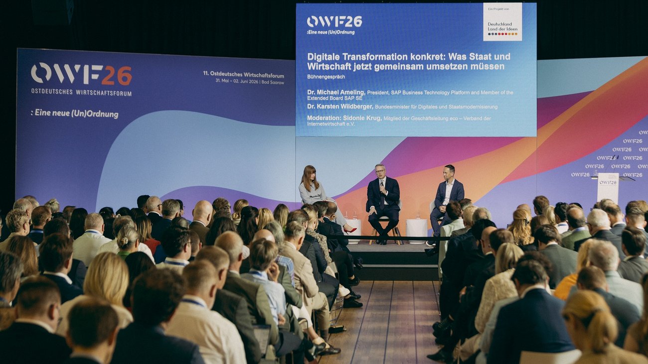 Auf einer Konferenzbühne vor großem Publikum sitzen drei Personen. Hinter ihnen ist eine Präsentationsfolie zum Ostdeutschen Wirtschaftsforum 2026 eingeblendet.